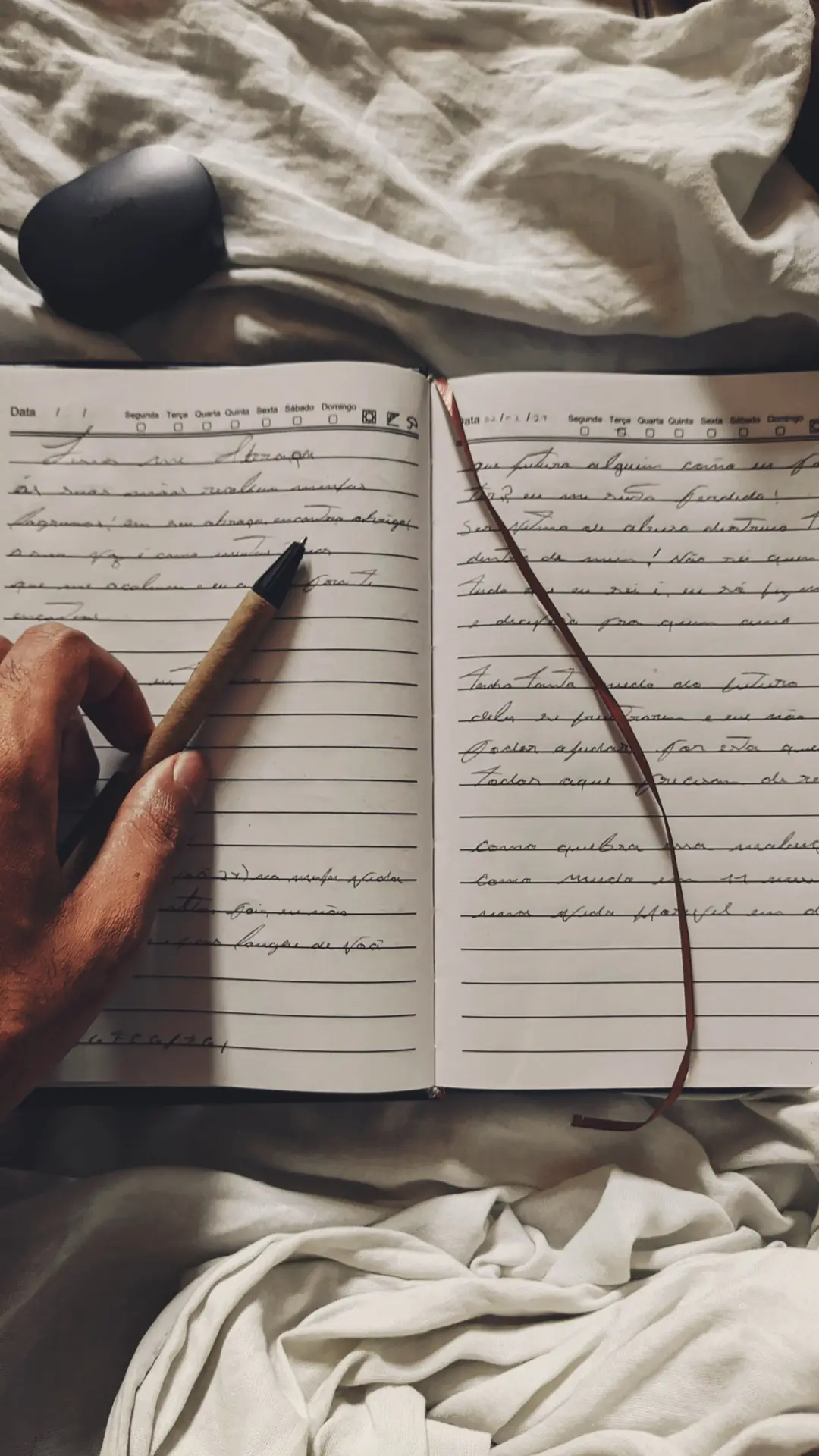 Journal ouvert et main tenant un stylo sur un lit