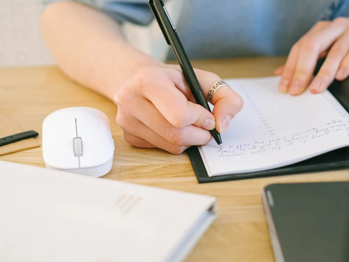 Main écrivant dans un carnet sur un bureau