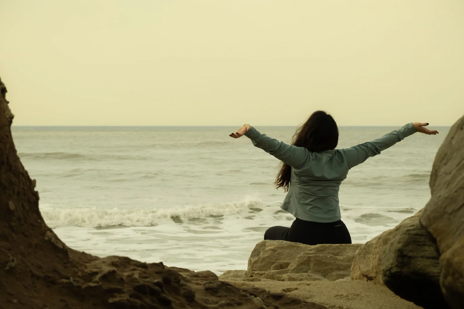 Femme assise face à la mer, les bras ouverts